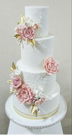 a three tiered white wedding cake with pink flowers on the top and gold trimmings