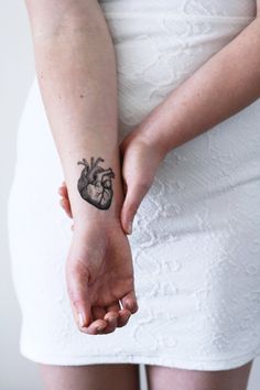 a woman with a heart tattoo on her arm holding the hand of a man who is wearing a white dress