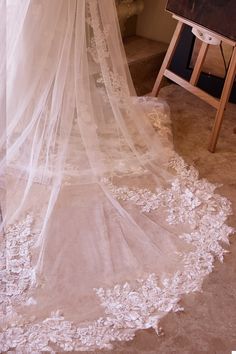 a white wedding veil hanging from the ceiling next to a painting on a easel