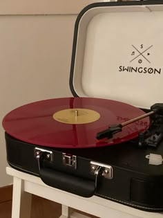 a red and black record player sitting on top of a white table next to a suitcase