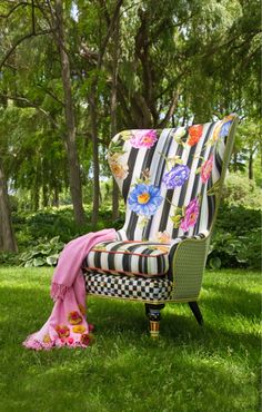 a striped chair sitting in the grass with a pink blanket on it's back