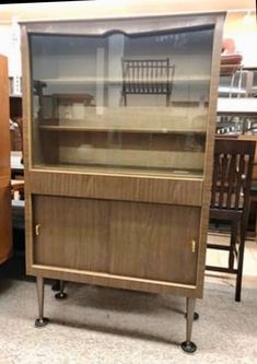 a wooden cabinet with glass doors and two chairs in the back, on display at a furniture store