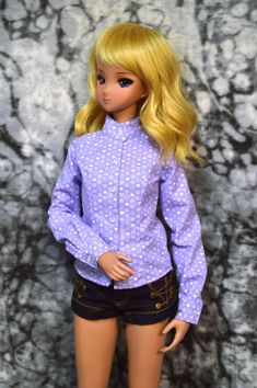 a doll with blonde hair wearing shorts and a purple shirt is standing in front of a wall