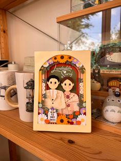 a card with two people on it sitting on a shelf next to coffee mugs