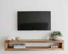 a flat screen tv mounted on the wall above a wooden shelf with books and vases