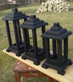 three black candlesticks sitting on top of a wooden table in the grass next to a pile of rocks