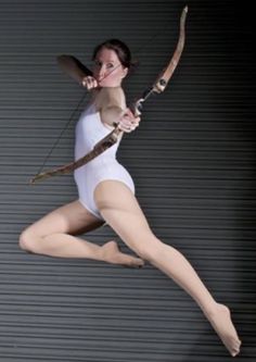 a woman in white leotard holding a bow and arrow with both hands while jumping up into the air