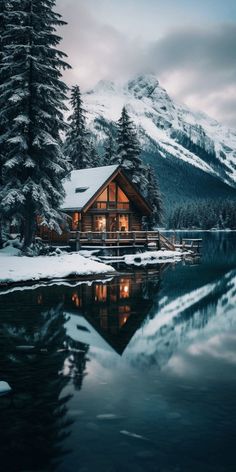 a cabin is lit up in the snow next to a body of water and trees