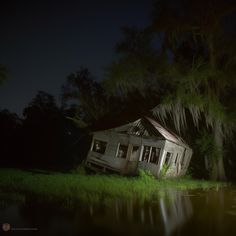 an old house sitting on the side of a river at night with moss hanging from it's roof