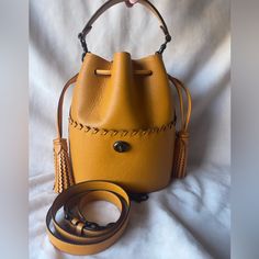 This Coach Lora Bucket Bag In Pollen Is A Must-Have For Any Fashion-Forward Woman. With Its Stylish Drawstring Design And High-Quality Leather Exterior And Interior, This Bag Is Perfect For Carrying All Your Essentials In Style While Also Being Extremely Durable. The Bag Has Been Well-Maintained And Is In Excellent Shape, Making It A Great Addition To Your Collection. There Is Only One Tiny Gray Speck On The Back Of The Bag (See Final Picture). The Pollen Color Is One Of Coach’s Most Popular And Coach Leather Bucket Bag With Removable Pouch, Coach Leather Bucket Bag For Daily Use, Yellow Bucket Bag With Gold-tone Hardware, Coach Bucket Bag For Everyday, Coach Leather Satchel Bucket Bag, Yellow Coach Leather Bag, Coach Leather Satchel Bag, Yellow Leather Bucket Satchel, Everyday Coach Bucket Bag