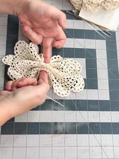 two hands are tying a piece of lace to a doily flower on a table