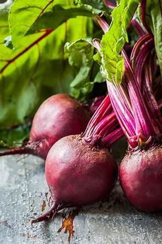 some beets are laying on the ground next to green leaves