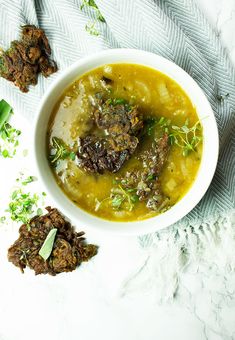 a white bowl filled with soup next to two pieces of meat on top of a table