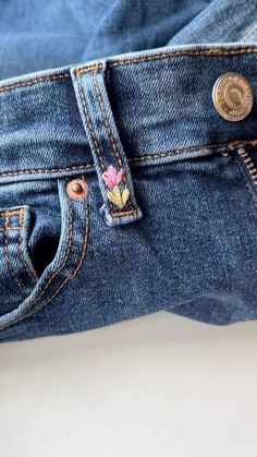 a pair of blue jeans with embroidered flowers on the back and side pockets, sitting on a white surface