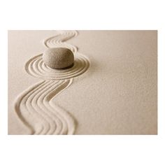 a rock sitting on top of a sandy beach next to a wave pattern in the sand