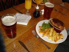 a table topped with plates of food and glasses of beer next to each other on top of a wooden table