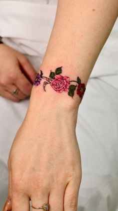 a woman's wrist tattoo with pink roses on it and green leaves in the middle