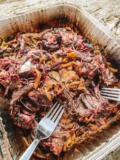 a container filled with meat and vegetables on top of a stone counter next to a fork