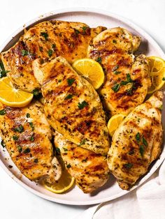 grilled chicken with lemons and herbs on a white platter, ready to be eaten