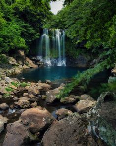 there is a waterfall in the middle of some rocks and green trees on either side