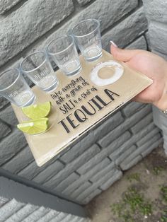 a person holding a tray with glasses and limes on it in front of a brick wall