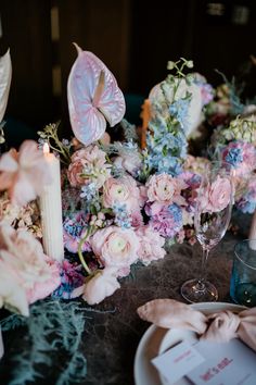 the table is set with pink and blue flowers, candles, and napkins on it