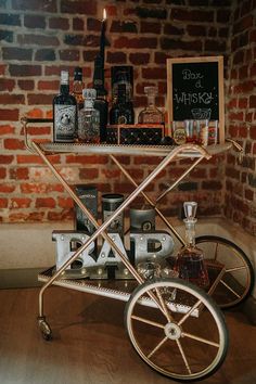 a bar cart sitting on top of a wooden floor next to a brick wall with liquor bottles