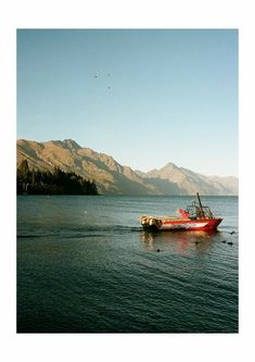 a red boat floating on top of a large body of water next to a mountain range