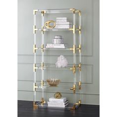 a glass shelf with gold handles and shelves on top of it, in front of a gray wall