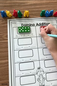 a child's hand holding a pencil and writing on a piece of paper with domino addition