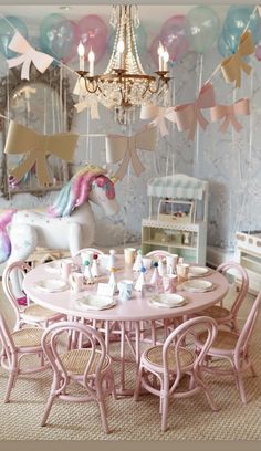 a pink table and chairs in a room with balloons on the ceiling, unicorn wallpaper