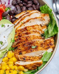 a bowl filled with chicken, lettuce, corn and black beans next to a fork