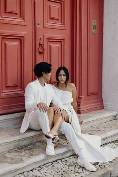 a man and woman sitting on steps next to each other in front of a red door