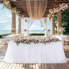 an outdoor wedding setup with white linens and pink flowers on the head table, overlooking the ocean