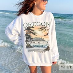 Our Oregon Pacific Northwest Sweatshirt--a cozy homage to the rugged charm of the Pacific Northwest! Crafted for comfort and warmth, this sweatshirt features a captivating watercolor scene of an Oregon sunset beachscape, complete with crashing waves, lush trees, and a soaring bald eagle.  Whether you're hiking, camping, or simply seeking a reminder of Oregon's wild beauty, this sweatshirt is the perfect companion. Embrace the spirit of the Pacific Northwest and carry a piece of its untamed allure with you wherever you go! .: Fabric blends: Heather Sport colors - 60% polyester, 40% cotton .: All others 50% cotton, 50% polyester .: Medium-heavy fabric (warm and cozy) .: Unisex loose fit - Please reference the size chart in the photos or feel free to reach out to me with any sizing questions! White Cotton Sweater For Outdoor, White Casual Sweater For Outdoor, White Relaxed Fit Sweatshirt For Outdoor Activities, Relaxed Fit Crew Neck Top For Weekend Getaway, Oregon Sunset, Beach Pullover, Wardrobe Makeover, Wild Beauty, Crashing Waves