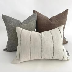 four pillows are lined up together on a white surface, one is gray and the other is brown