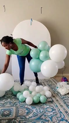 a woman standing on top of a bed surrounded by white and green balloons in the air