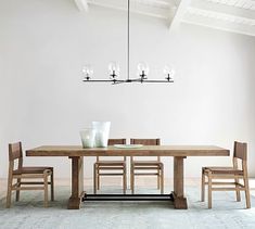 a dining room table and chairs in front of a white wall with a chandelier