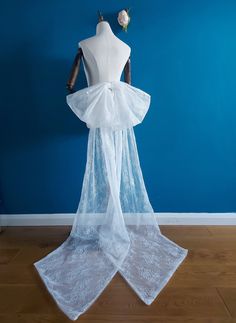 a mannequin wearing a white veil with flowers on the head and neck, in front of a blue wall