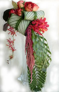 a vase filled with flowers and greenery on top of a white table next to a wall