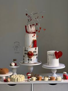 three tiered cakes and desserts on display in front of a white wall with red hearts