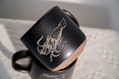 a black coffee mug with an octopus on it's side sitting on a white towel