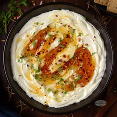 a black plate topped with mashed potatoes covered in sauce and green garnish