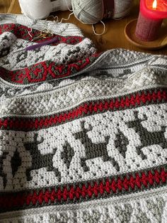 a crocheted afghan sits on a table next to a candle and some yarn