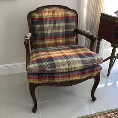 an old chair with plaid upholstered seat and arm rests in front of a window