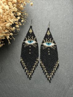 These long black beaded earrings are an amazing blend of sophistication and style. Made from high-quality materials, they are adorned with an eye ornament symbolizing protection and luck. Golden accents add sophistication and sparkle, making them a beautiful addition to your look. These unique earrings will accentuate your individuality, attracting admiring glances from those around you. Made from Czech beads. Hypoallergenic clasp. Length 4.8 inches (12,3 cm). Width 1.3 inches (3.3 cm). If you w Fringe Bead Earrings, Eye Ornament, Gold Beaded Earrings, Native Earrings, Gold Bead Earrings, Evil Eye Earrings, Jewelry Black, Eye Earrings, Earrings Long