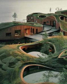 an unusual house with grass growing on the roof and walls, in front of a body of water