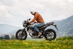 a man riding on the back of a motorcycle down a lush green field covered in yellow flowers