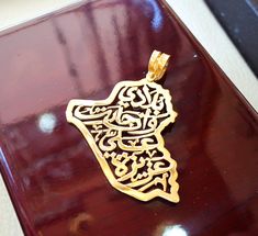 a gold pendant with an intricate design on top of a wooden table in a room