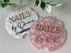 two pink and gold nails by rrl signs on a white surface with green leaves